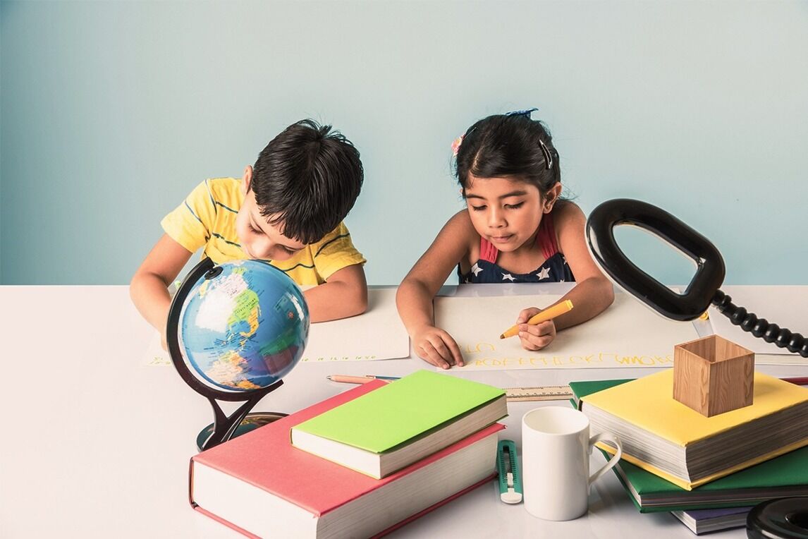 Young boy and girl studying at a desk with books and a globe